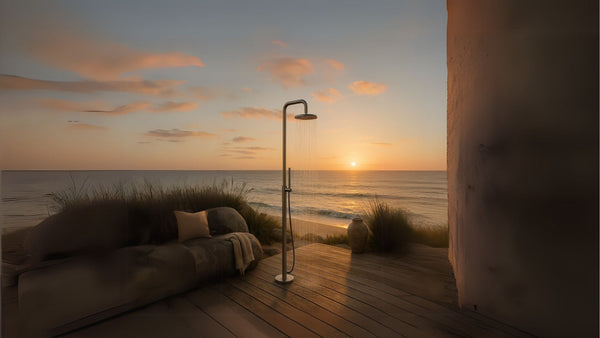 Outdoor shower made of brushed stainless steel on a wooden deck overlooking the ocean at sunset.